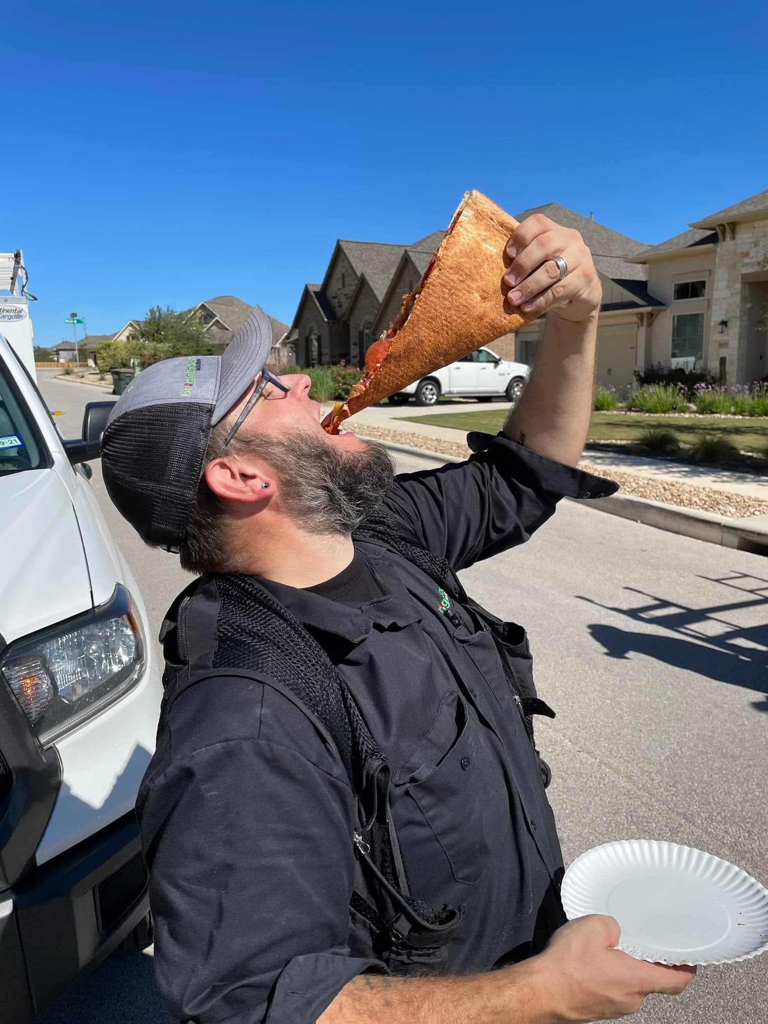 An installer tipping his head back to lower a giant slice of pizza into his mouth, paper plate in his other hand.
