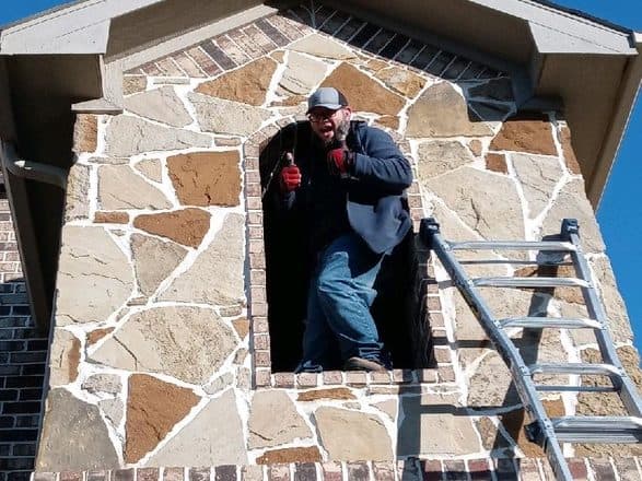 An installer standing in the open stone alcove of a turret two stories up, ladder leaned beside him, mid-job.