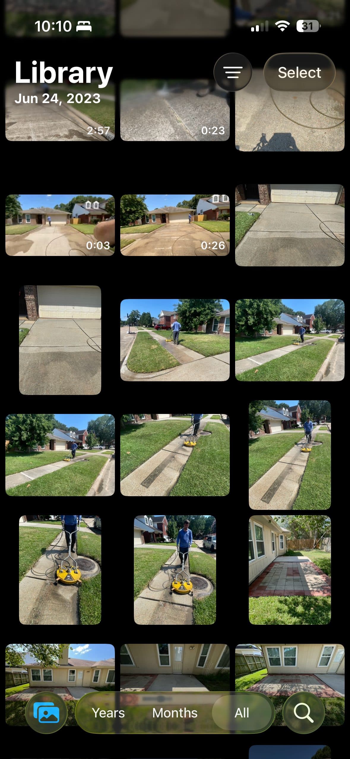 A phone camera roll from a 2023 job day: a wall of near-identical pressure washing photos and videos — driveways, sidewalks, a surface cleaner mid-pass — with the pair that matters buried somewhere in it.